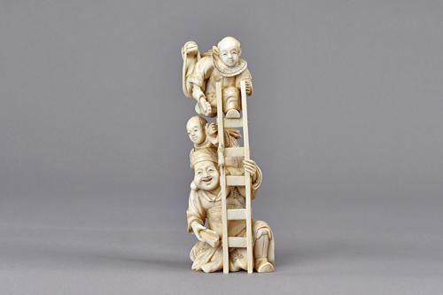A Japanese ivory okimono, Meiji period, carved as a seated Daikoku holding a ladder, one child clambering up his back, another above carrying a hobby