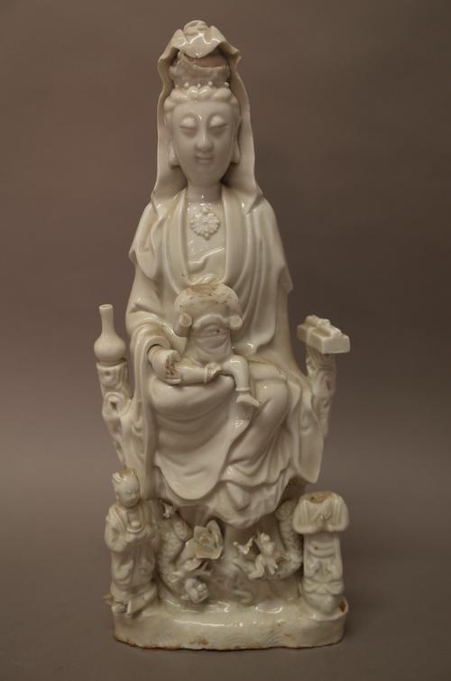 A Chinese blanc de chine figure of Guanyin, 18th/19th century, modelled seated with a boy on her lap and two acolytes standing below, (a.f), 37cm. hig