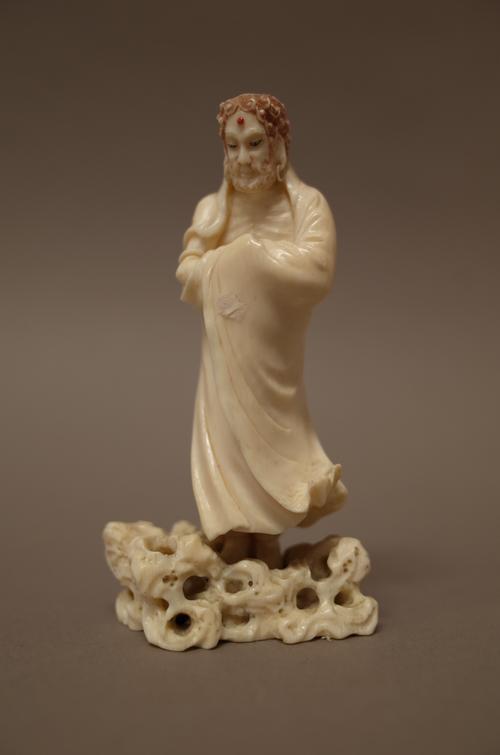 A small Japanese ivory figure of a deity, Meiji period, standing in long robes with arms folded, on a pierced rockwork base, signed, 10cm. high.