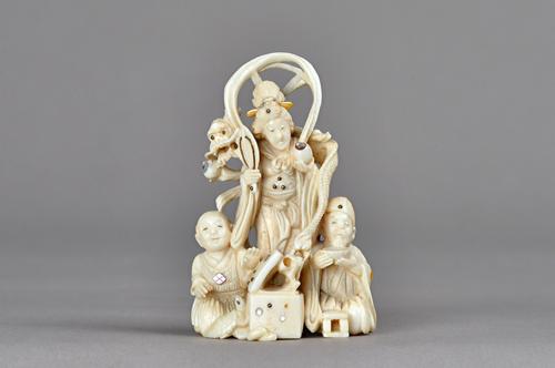 A small Japanese ivory and mother-of-pearl inlaid okimono, Meiji period, carved as Kannon standing with a dragon across her shoulders, two attendants