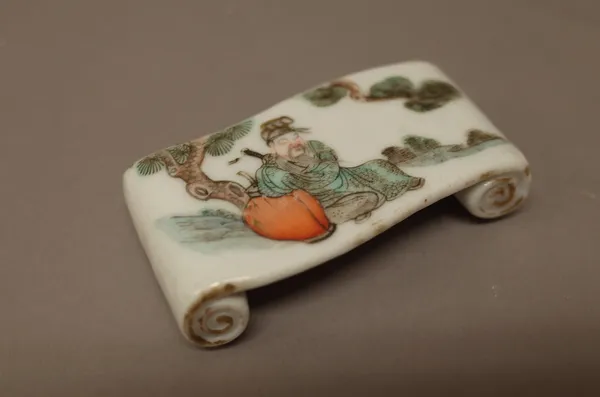 A Chinese porcelain brush rest, 19th century, in the form of a scroll, painted in a famille-verte palette with a figure seated beneath a pine tree, 7.