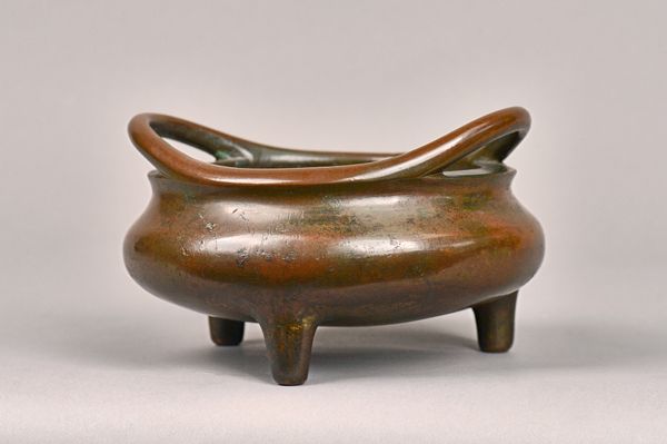 A Chinese bronze tripod censer, Xuande sixteen character mark but probably 17th/18th century, of compressed form with loop handles, 19.5cm. wide. Illu