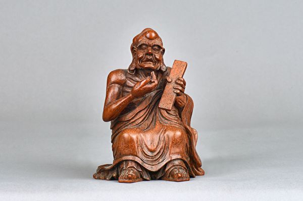 A Chinese bamboo figure of a luohan, carved seated in loose robes, holding a tablet in his left hand, 14cm.high. Illustrated. Provenance; From a disti