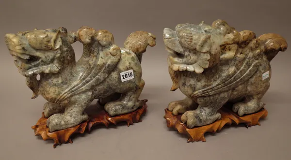 A large pair of Chinese jade figures of standing winged mythical creatures, 20th century, the stone of grey, brown and grey tones, 33cm. length, wood