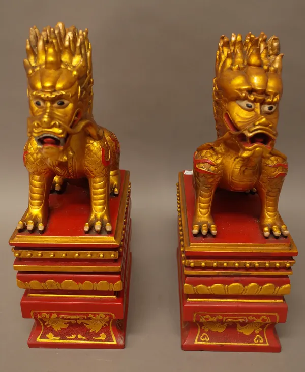 A pair of Chinese gilt and red painted stone figures of dragons, 20th century, each modelled seated on a rectangular plinth, 46cm. high, (2).