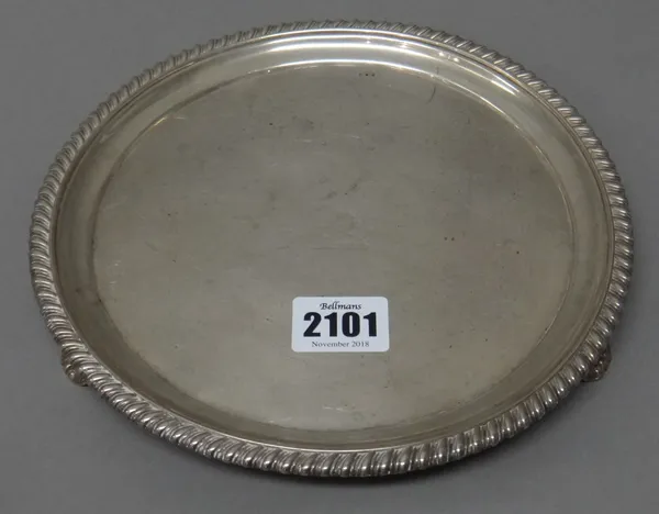 A George IV silver salver, of circular form, crest engraved to the centre and with a gadrooned rim, raised on three feet, having floral and scallop sh