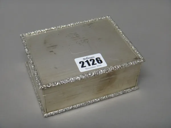 A silver rectangular table cigarette box, wooden lined within, the exterior engine turned within floral moulded borders and with a vacant cartouche to