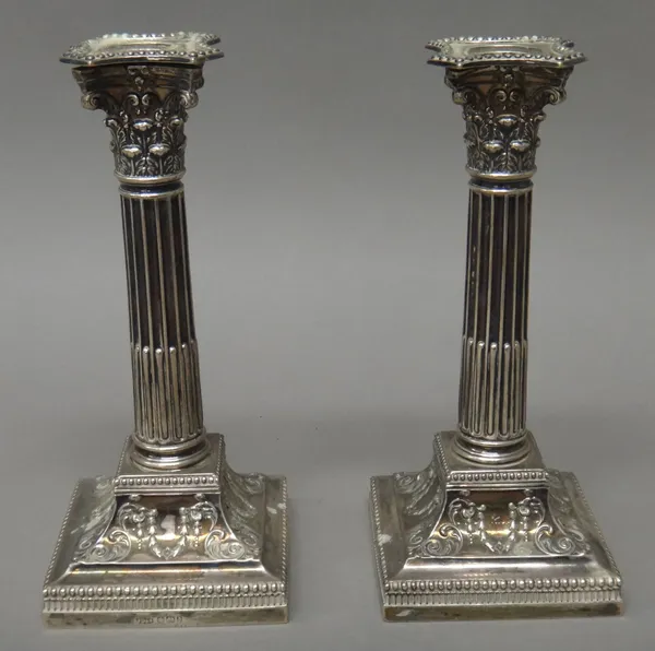 A pair of late Victorian silver table candlesticks, each of Corinthian column form, raised on a scroll and festoon decorated square base, with beaded