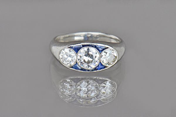 A platinum, diamond and synthetic sapphire ring, collet set with the three princpal cushion shaped diamonds to the centre, the diamonds weigh in total