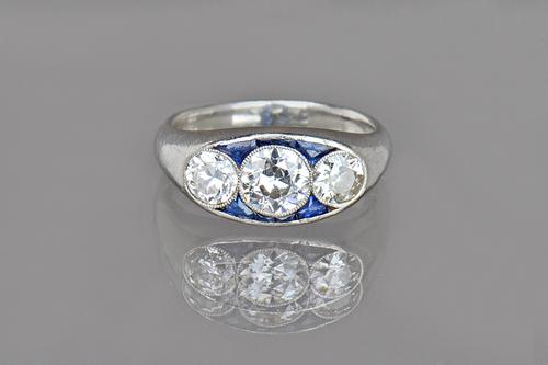 A platinum, diamond and synthetic sapphire ring, collet set with the three princpal cushion shaped diamonds to the centre, the diamonds weigh in total