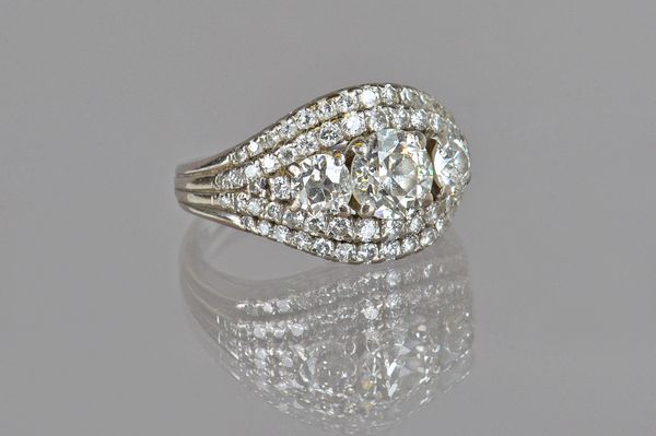 A diamond ring, claw set with the three principal cushion shaped diamonds to the centre, between circular cut diamond set two row sides, in a domed de