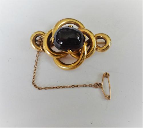 A Victorian gold and carbuncle garnet set brooch, in an entwined design, claw set with the oval carbuncle garnet to the centre, the back glazed with a