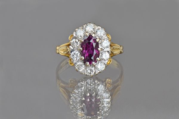 An 18ct gold, ruby and diamond oval cluster ring, claw set with the oval cut ruby to the centre in a surround of ten circular cut diamonds between scr