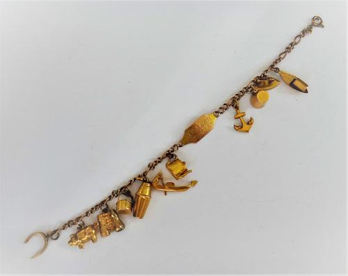 A gold identity bracelet, fitted with ten mostly gold charms, including an anchor, a mug and a pig, gross weight 13.9 gms.