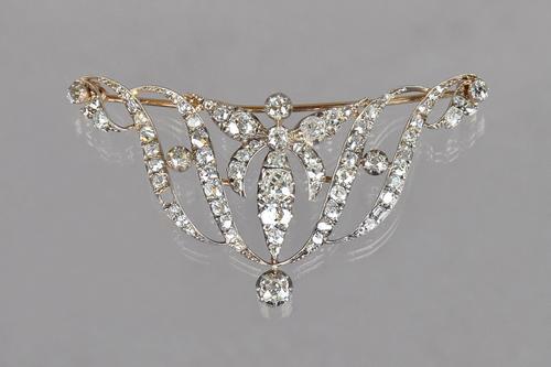 A Victorian diamond brooch, in a shallow scrolling openwork design, mounted with cushion shaped and rose cut diamonds, (one diamond lacking), length 6