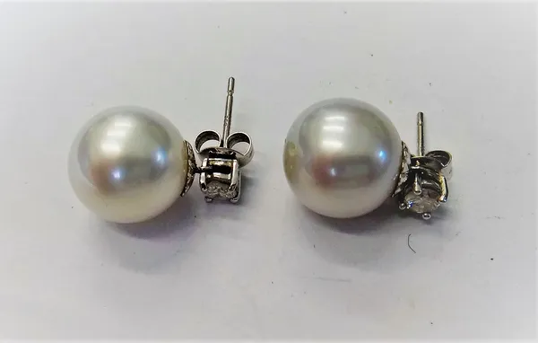 A pair of white gold, cultured pearl and diamond earrings, each claw set with a circular cut diamond above a single cultured pearl, the backs with pos