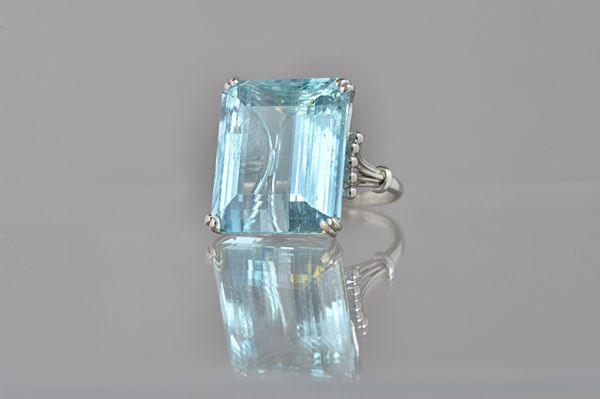 An aquamarine single stone ring, claw set with a large cut cornered rectangular step cut aquamarine, between beaded wirework shoulders, ring size M. I