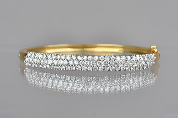 A gold and diamond set oval hinged bangle, mounted with three rows of circular cut diamonds, on a snap clasp, with a foldover safety catch, detailed 1