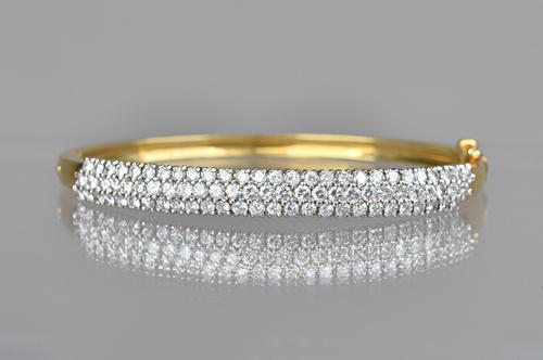 A gold and diamond set oval hinged bangle, mounted with three rows of circular cut diamonds, on a snap clasp, with a foldover safety catch, detailed 1