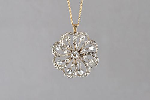 A diamond pendant, in a shaped circular scrolling design, mounted with cushion shaped and rose cut diamonds and with the principal diamond mounted at