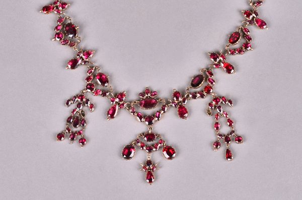 A gold and foil backed flat cut garnet set necklace, first half of the 19th century, in a drop and pendant swag openwork design, the front with three