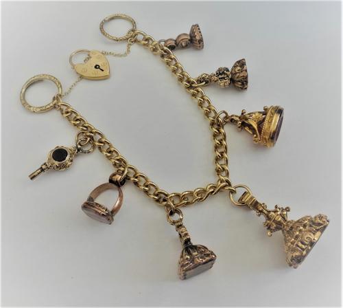 A curb link charm bracelet, with a heart shaped padlock clasp, detailed 9 CT, fitted with six pendant fob seals, a gem set watch key and with two spli
