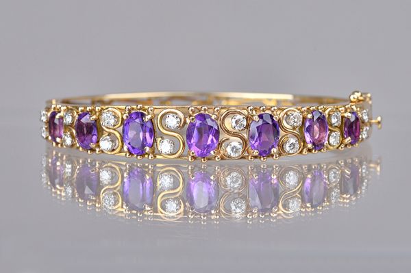 A gold, amethyst and diamond set oval hinged bangle, the front mounted with a row of seven graduated oval cut amethysts and with eight pairs of circul