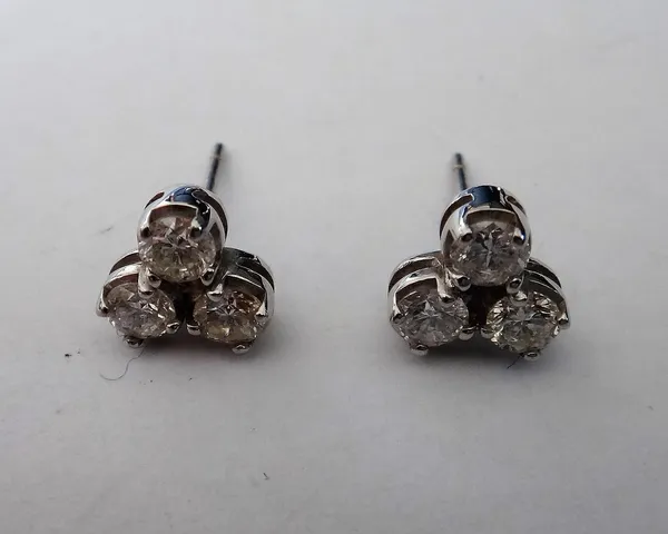A pair of white gold and diamond three stone ear studs, each claw set with circular cut diamonds, the posts detailed 750 (the butterfly clips lacking)