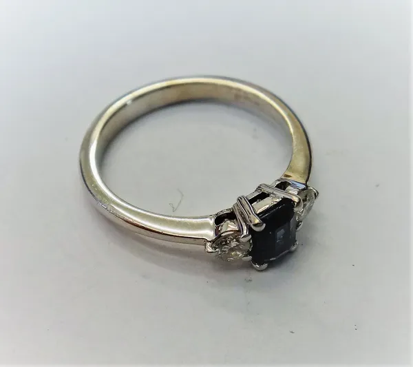 An 18ct white gold, sapphire and diamond three stone ring, claw set with the rectangular emerald cut sapphire at the centre, between two circular cut
