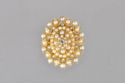 A Victorian gold, diamond and half pearl set oval brooch, mounted with the cushion shaped diamond at the centre and otherwise mounted with half pearls