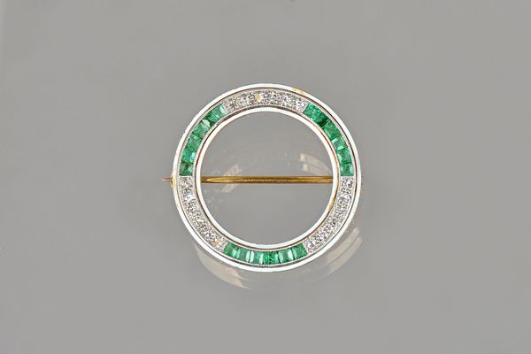 A gold and platinum, emerald and diamond set brooch, in an openwork circular design, mounted with rows of calibre cut emeralds, alternating with rows