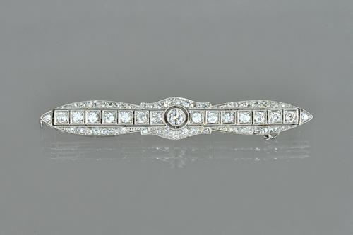 A diamond brooch of shaped tapered form, collet set with the principal cushion shaped diamond to the centre, between two rows of smaller cushion shape