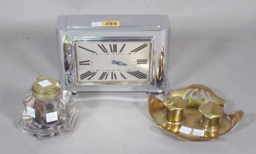 An early 20th century chrome Art Deco eight day clock, 20cm wide x 13cm high, a brass Art Deco inkwell and a glass octagonal ink well, (3).   CAB