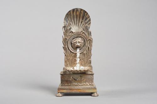 A silvered brass automata watch standIn the Empire styleModelled with a scallop shell above bullrushes, centred by a lion mask 'fountain' head, with s