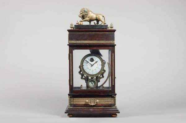 A giltmetal-mounted stained wood rolling ball timepiece20th Century Surmounted by a figure of a lion with four finials, above a panel door, with pull-