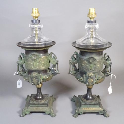A pair of wooden bronze and glass table lamps, each of two handled urn form, Renaissance style with a green patina on a square base and four lion paw