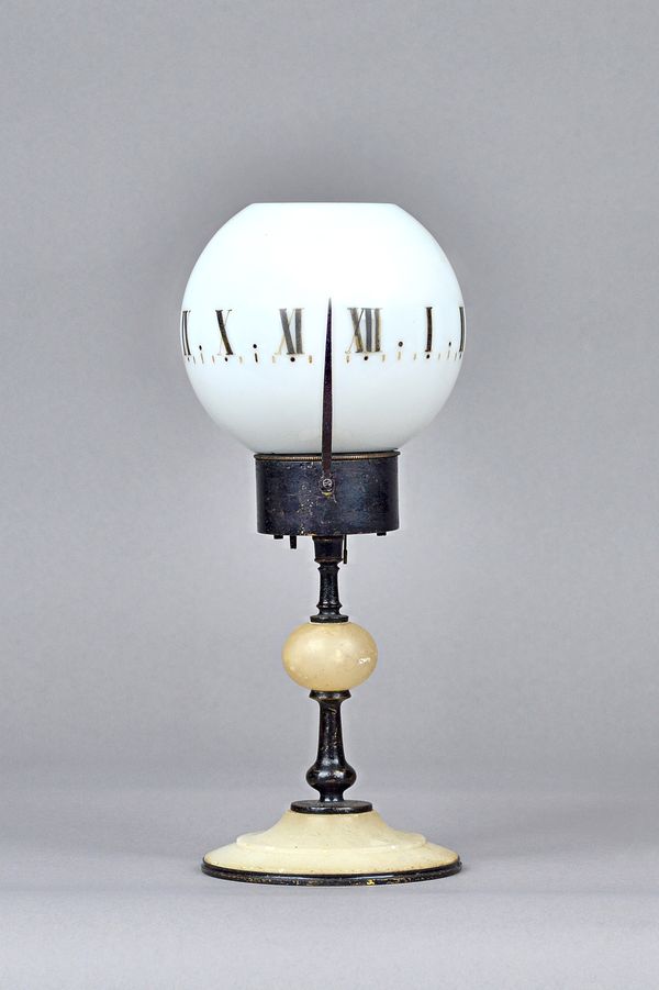 A candle clock, early 20th century, with opaque glass globular shade, brass cased movement and a knopped brass and alabaster foot, 24cm high.  Illustr