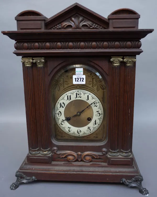 A German early 20th century, mahogany cased mantel clock, with apex surmount over a foliate engraved brass dial plate, flanked by carved Corinthian pi