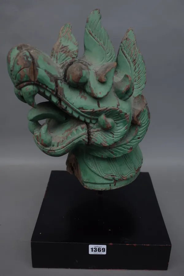A green painted carved wooden Chinese dragon head, distressed, raised on an ebonised wooden square plinth, 45cm high overall.