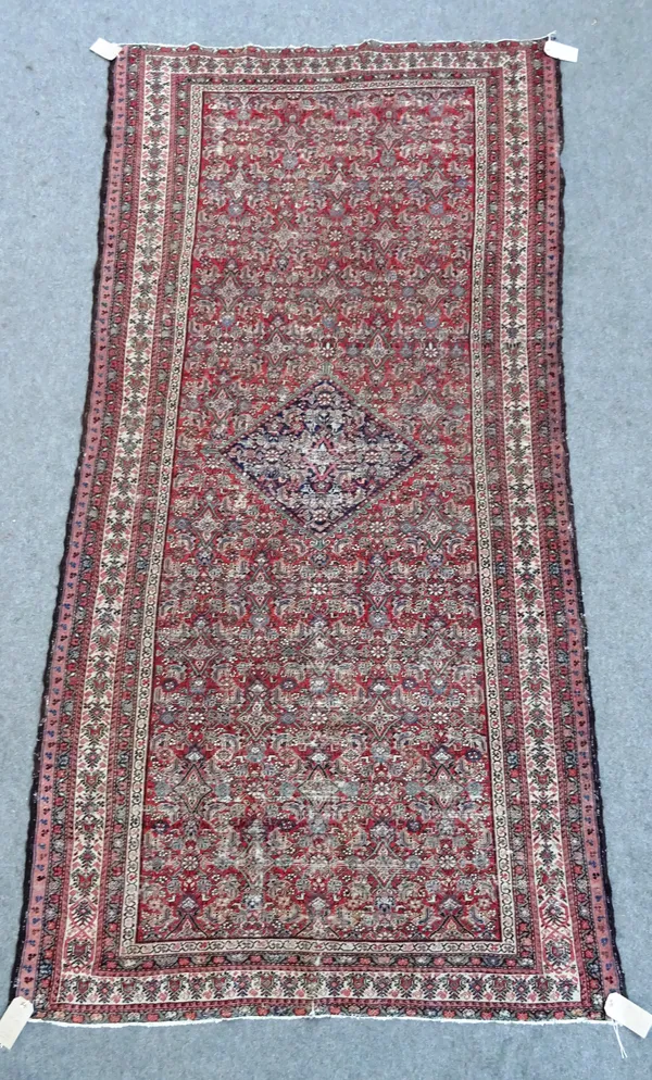 A Senneh rug, Persian, the madder field with a central indigo diamond, all with an intricate herate design; an ivory tulip border, 285cm x 143cm.