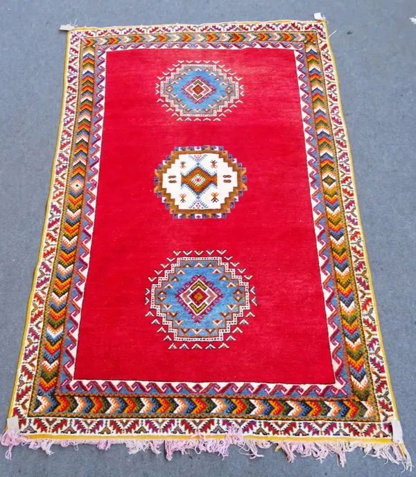 A Moroccan carpet, North African, the plain madder field with three single medallions, a chevron border, 298cm x 198cm.