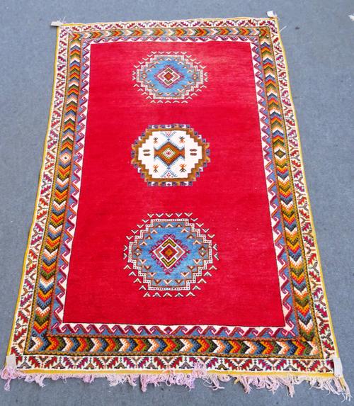 A Moroccan carpet, North African, the plain madder field with three single medallions, a chevron border, 298cm x 198cm.