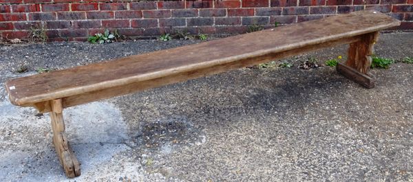 A early 19th century pitch pine bench, on a pair of double staked silhouette supports, 238cm wide x 44cm high x 33cm wide.    Provenance; Property fro