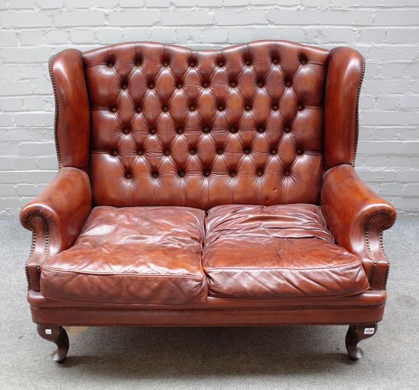 An 18th century style studded brown leather upholstered two seat wingback sofa on squat cabriole supports, 124cm wide x 96cm high.