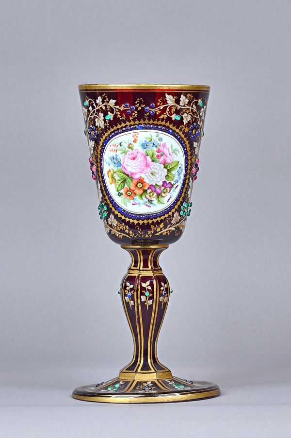 A Bohemian ruby glass enamelled chalice, late 19th century, with foliate painted enamel oval, bordered by coloured jewels against a gilt foliate groun