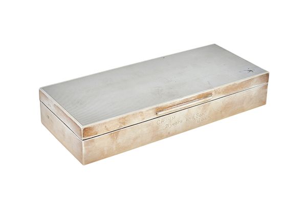 A silver rectangular, hinge lidded table cigarette box, wooden lined within, the lid engine turned, the front inscribed Crimm 21 Years & Son Joan, len