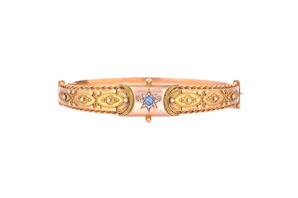 A 9ct gold, diamond and sapphire set oval hinged bangle, the front with a starburst shaped motif, centred by a cushion shaped sapphire, in a surround