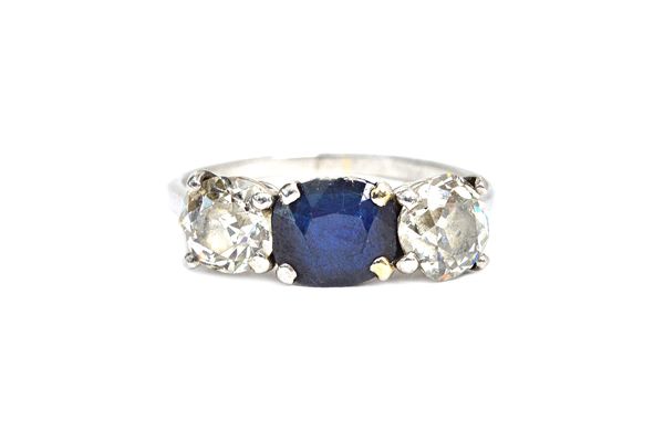 A diamond and sapphire three stone ring, claw set with an oval cut sapphire at the centre, between two cushion shaped diamonds, ring size P and a half