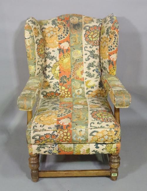 A 20th century oak framed wingback open armchair on ring turned supports and floral upholstery.   K3
