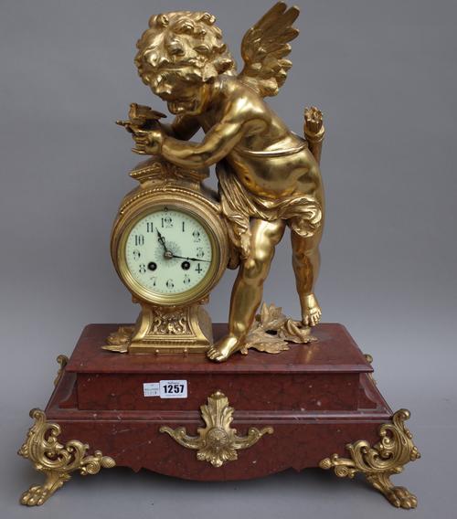 A French gilt metal mounted rouge marble figural mantel clock, early 20th century, the cupid figure resting on a drum case over a marble base and four